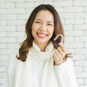 Woman in sweater smiling and holding Invisalign aligner