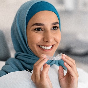 Woman in dental chair smiling and holding a clear aligner