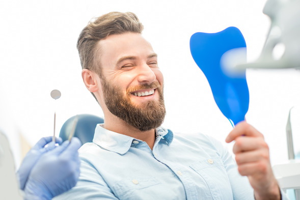 man smiling while holding dental mirror 